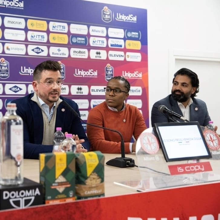 Four people sit in front of a conference table with microphones in front of them to take questions.