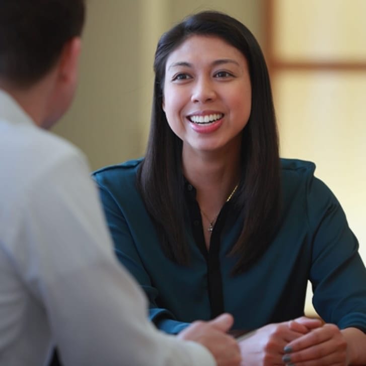 A woman in a blue formal shirt talks at a table with a man in a white button-down shirt.