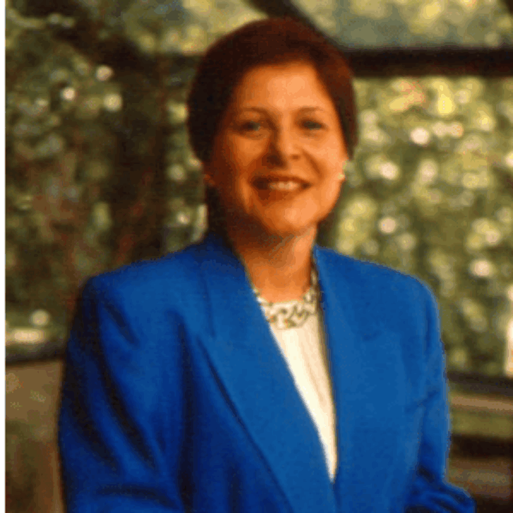 Janice Ballice is wearing a blue suit with a white shirt. She stands behind a chair.