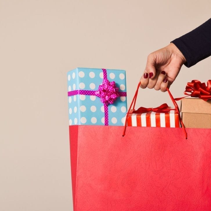 A woman holding a gift bag with three wrapped presents sticking out.