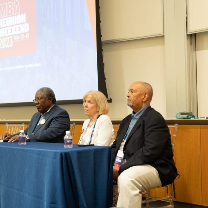 Members of the class of 1973 seated in front a table with a blue tablecloth for a panel discussion.