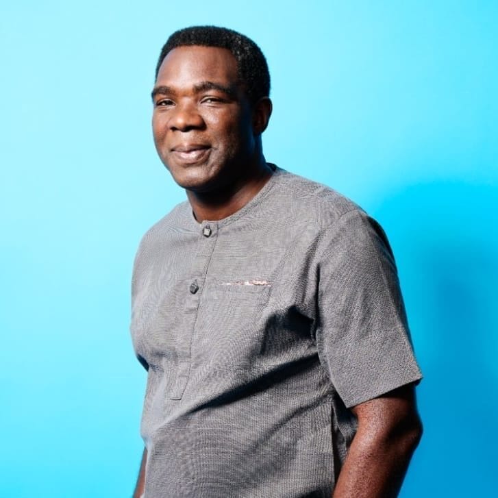 Portrait of alumnus Femi Badeji standing in front of a bright blue background.