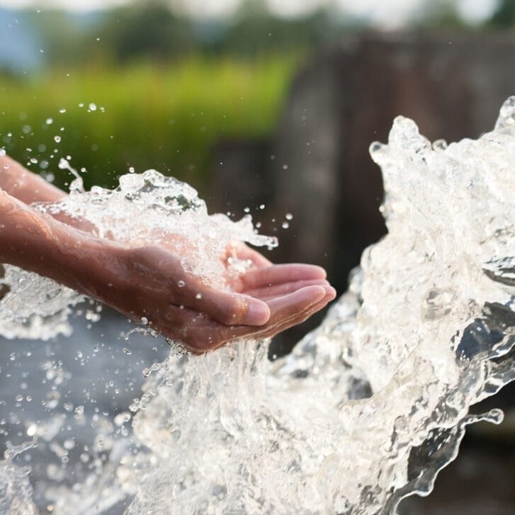 Hands cupped in front of a splash of water in a lake.