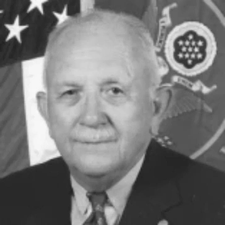 Man poses in a suit and tie in front of an American flag.