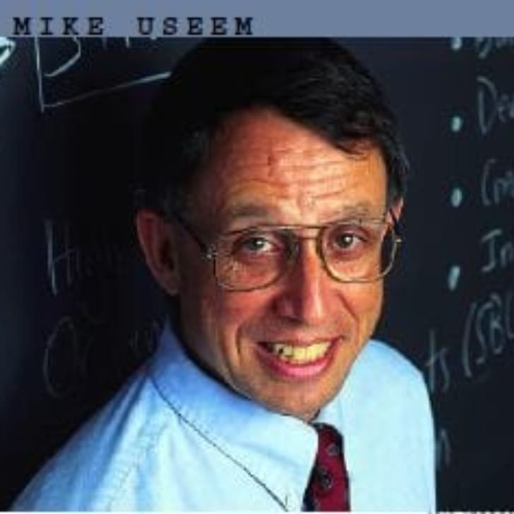 A smiling man standing in front of a chalkboard.