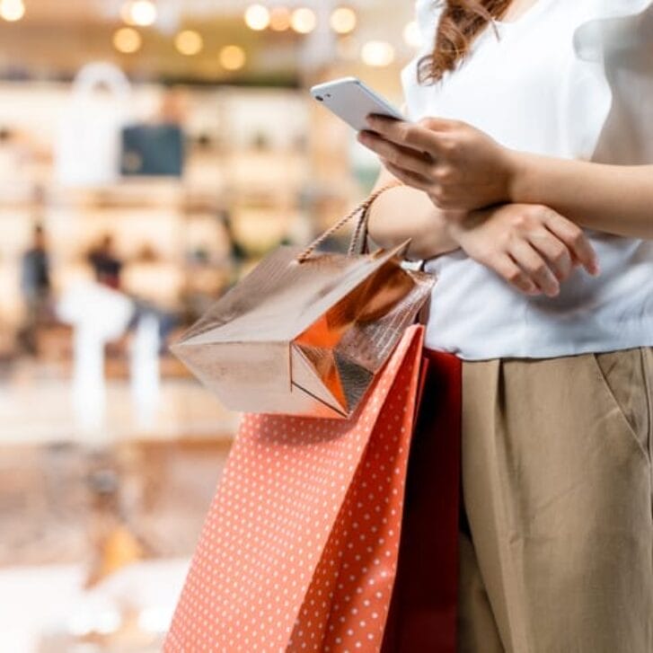 A woman using her smartphone and holding holiday shopping bags.