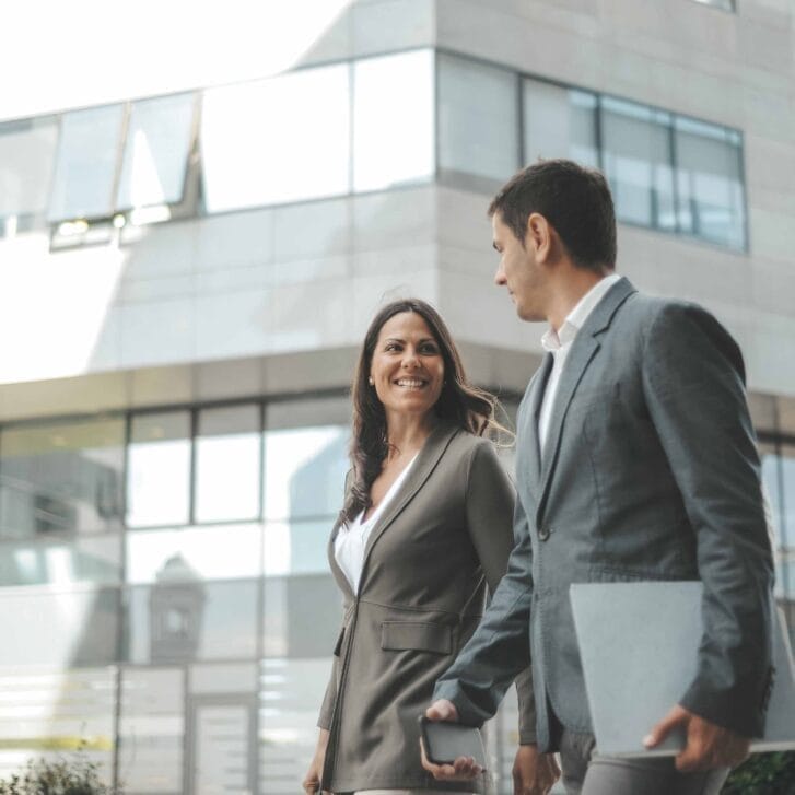 Man and woman in business attire walking side by side near office buildings