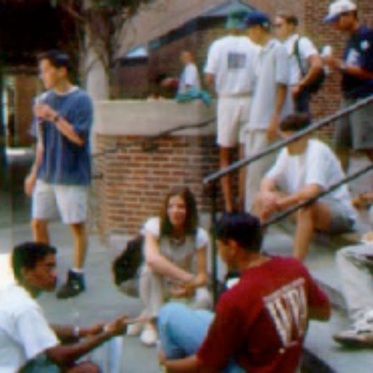 Students sit and stand on steps of a building.