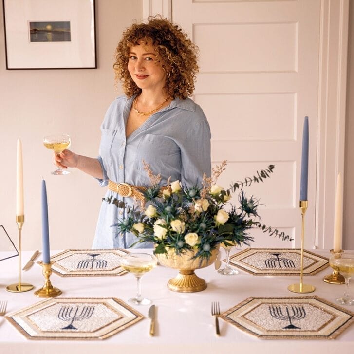 Portrait of a woman standing in front of a table adorned with Jewish decor.