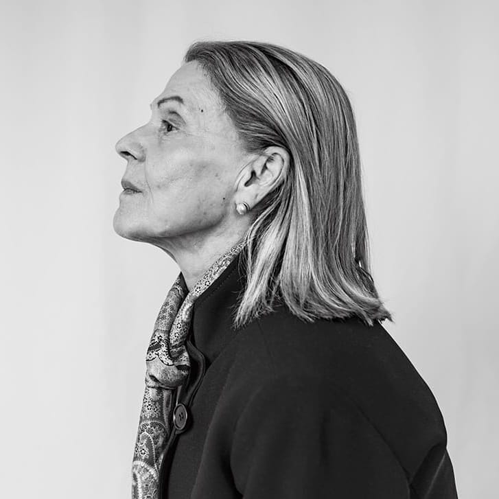 Portrait of a woman with straight hair facing sideways and wearing a black jacket and a patterned scarf.