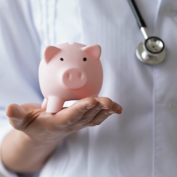 Person wearing a stethoscope and holding a piggy bank