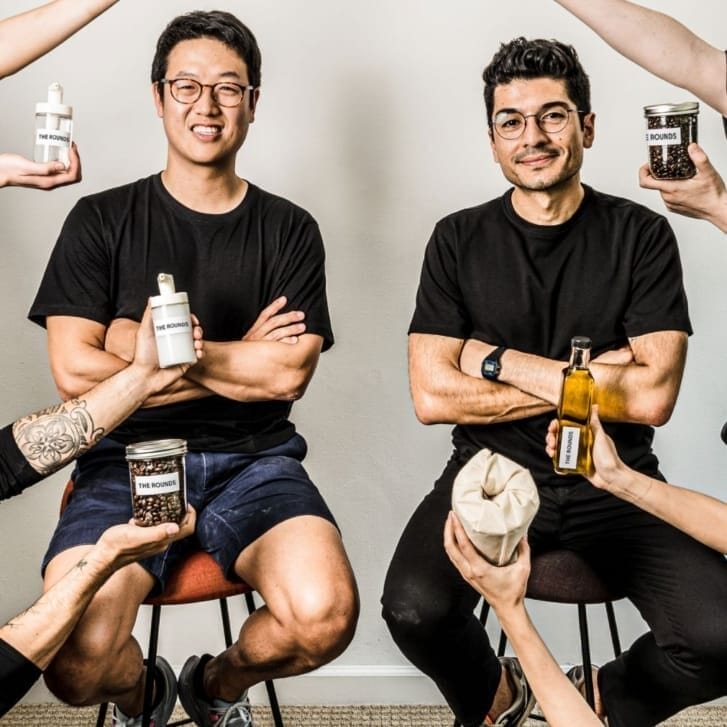 Portrait of Byungwoo Ko and Alex Torrey surrounded by hands holding up products packed by The Rounds.