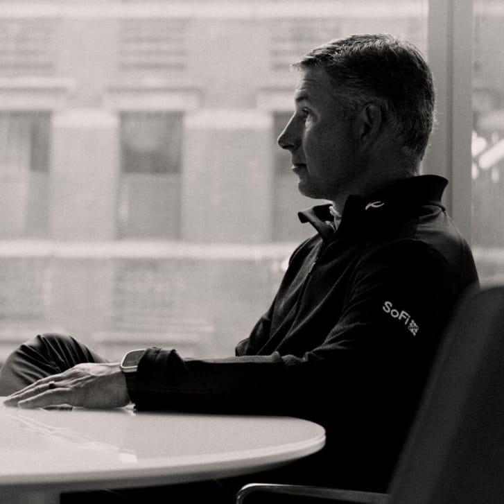 Portrait of Social Finance CEO Anthony Noto seated facing the left and wearing a quarter-zip shirt with the SoFi logo on the left arm.