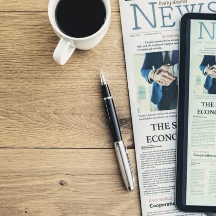 Newspaper and digital tablet on wooden table.