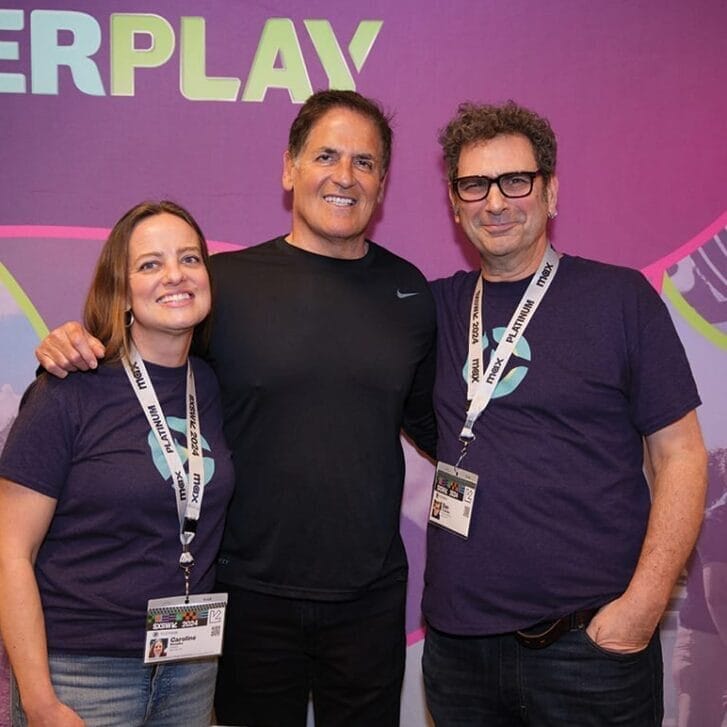 Three people pose for a photo together against a backdrop with imagery for the startup Overplay on it.