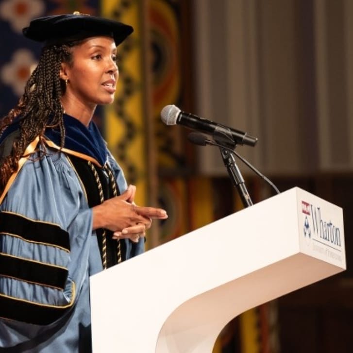 Dean Erika James speaks at a podium in commencement attire.