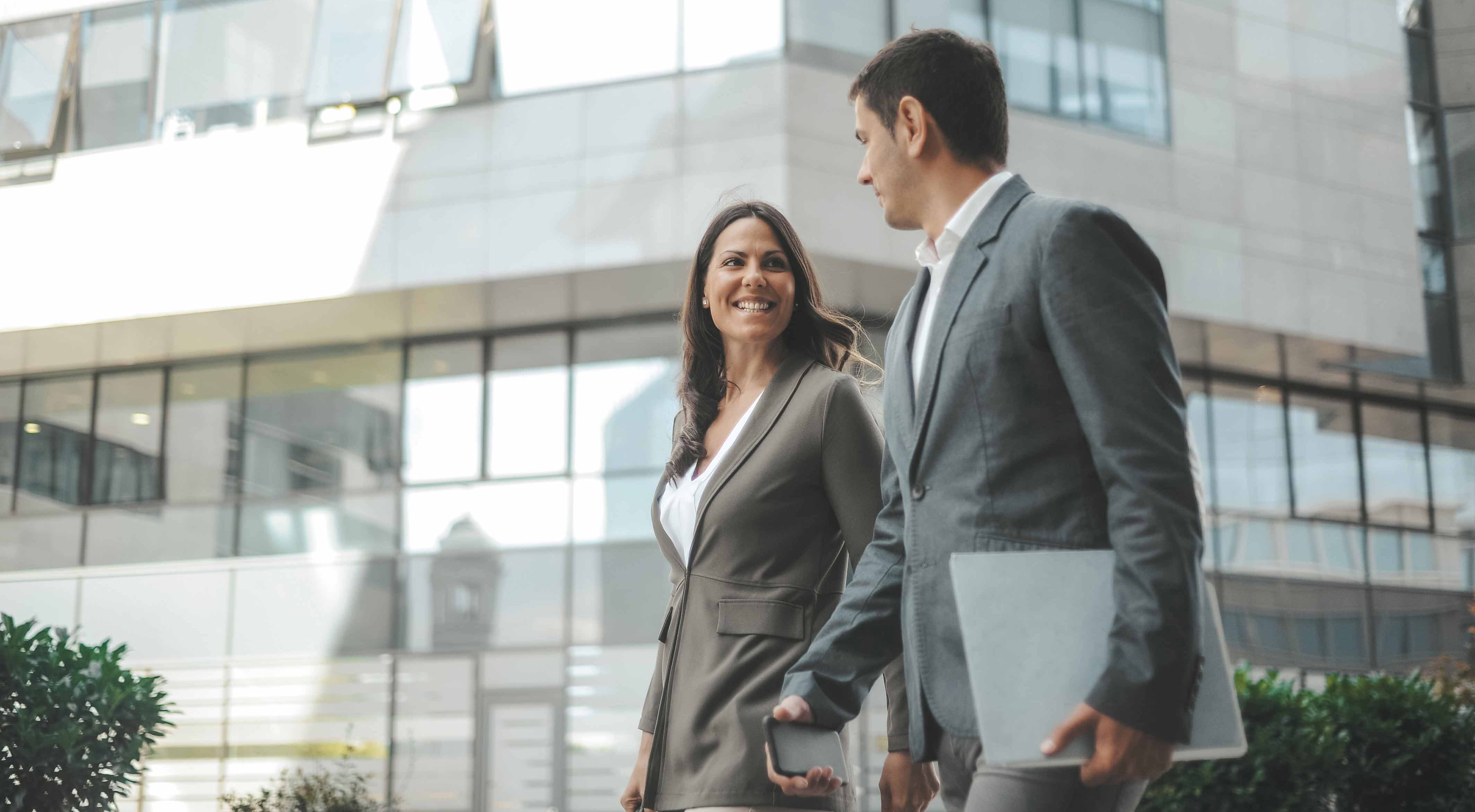 Man and woman in business attire walking side by side near office buildings