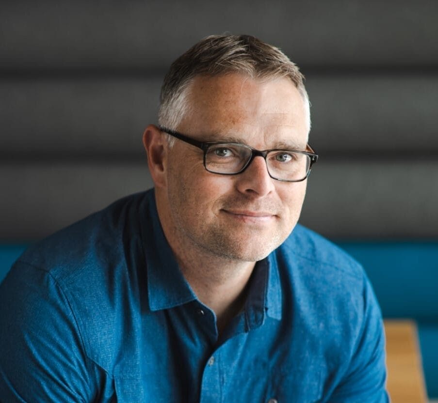 Man wearing a blue button-down shirt and black-rimmed glasses.