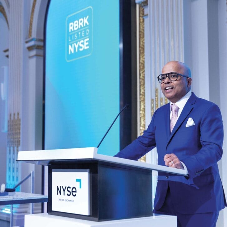 A man in a blue suit stands at a podium at the New York Stock Exchange.