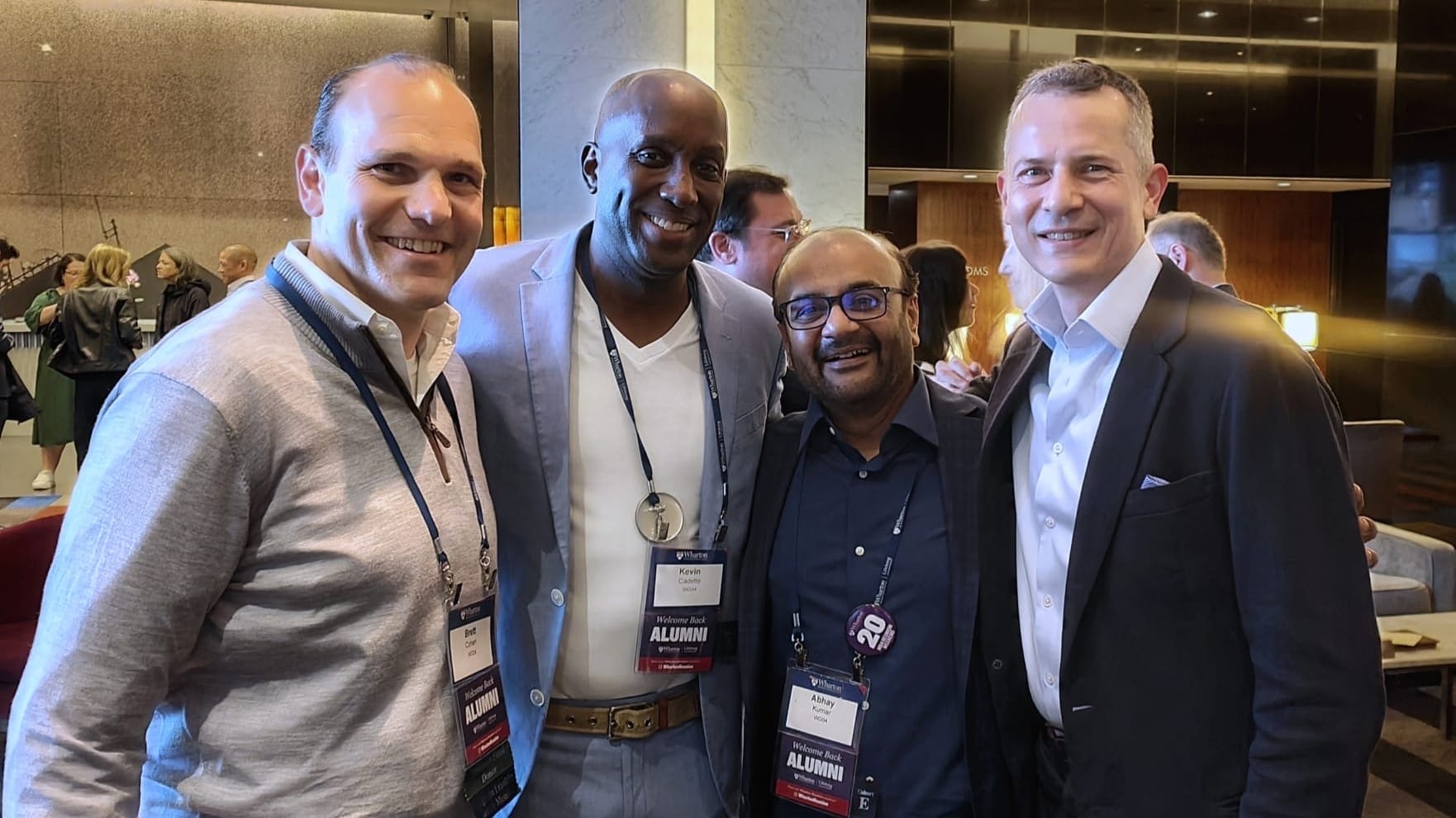 Four alumni in business attire pose together for a photo.