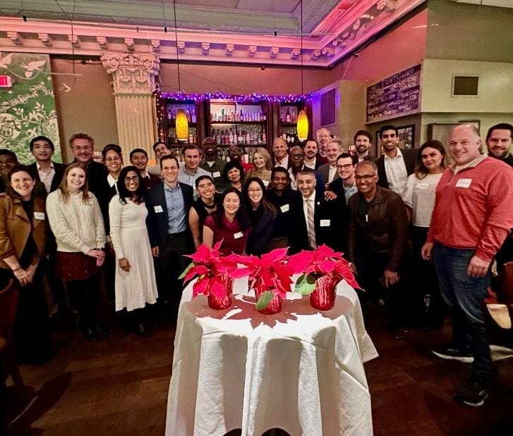 Dozens of alumni pose together at a restaurant with holiday flowers in front of them.