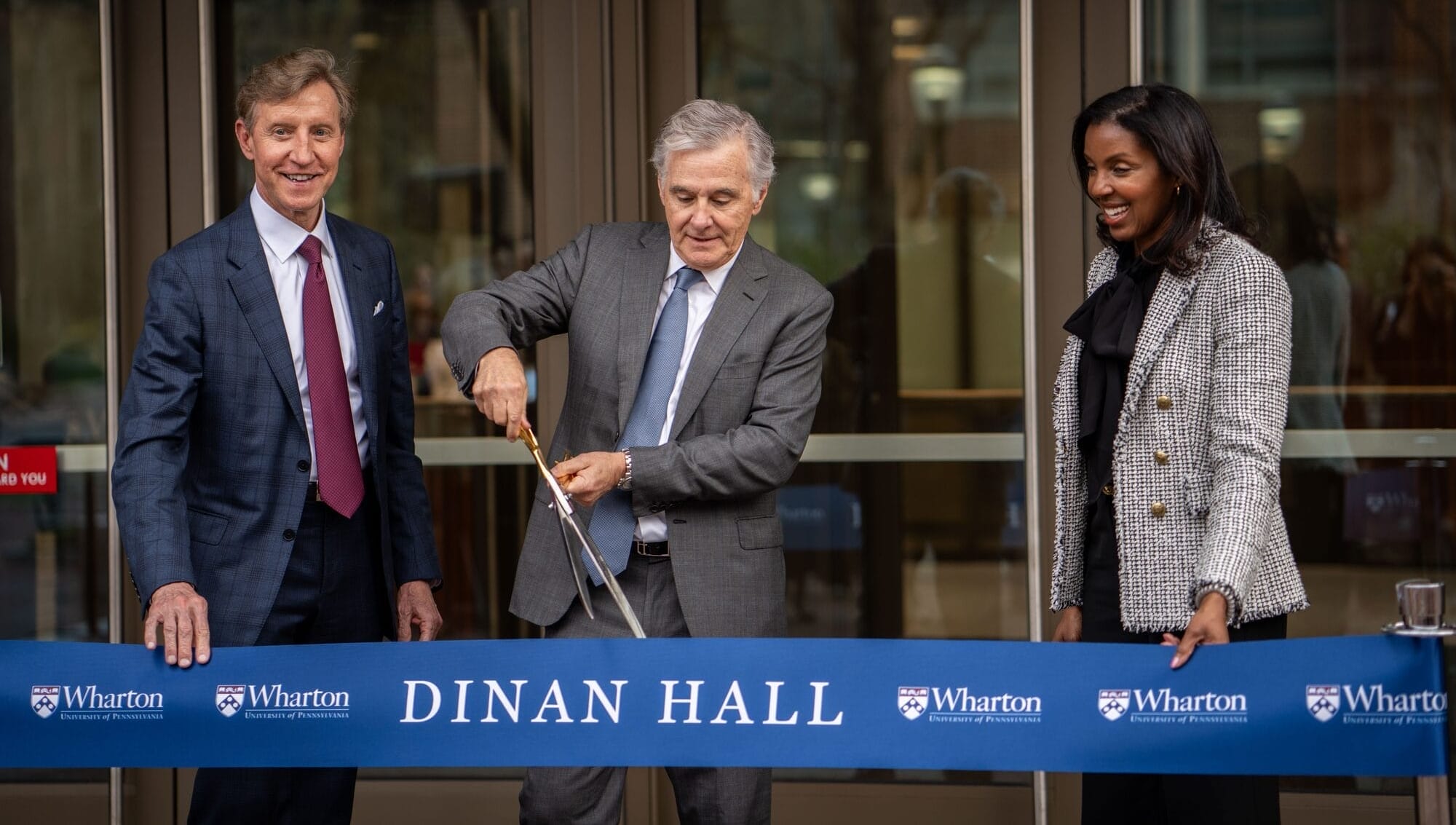 Jamie Dinan W81 cuts a giant ribbon as Dean Erika James and Penn President Larry Jameson stand on either side of him
