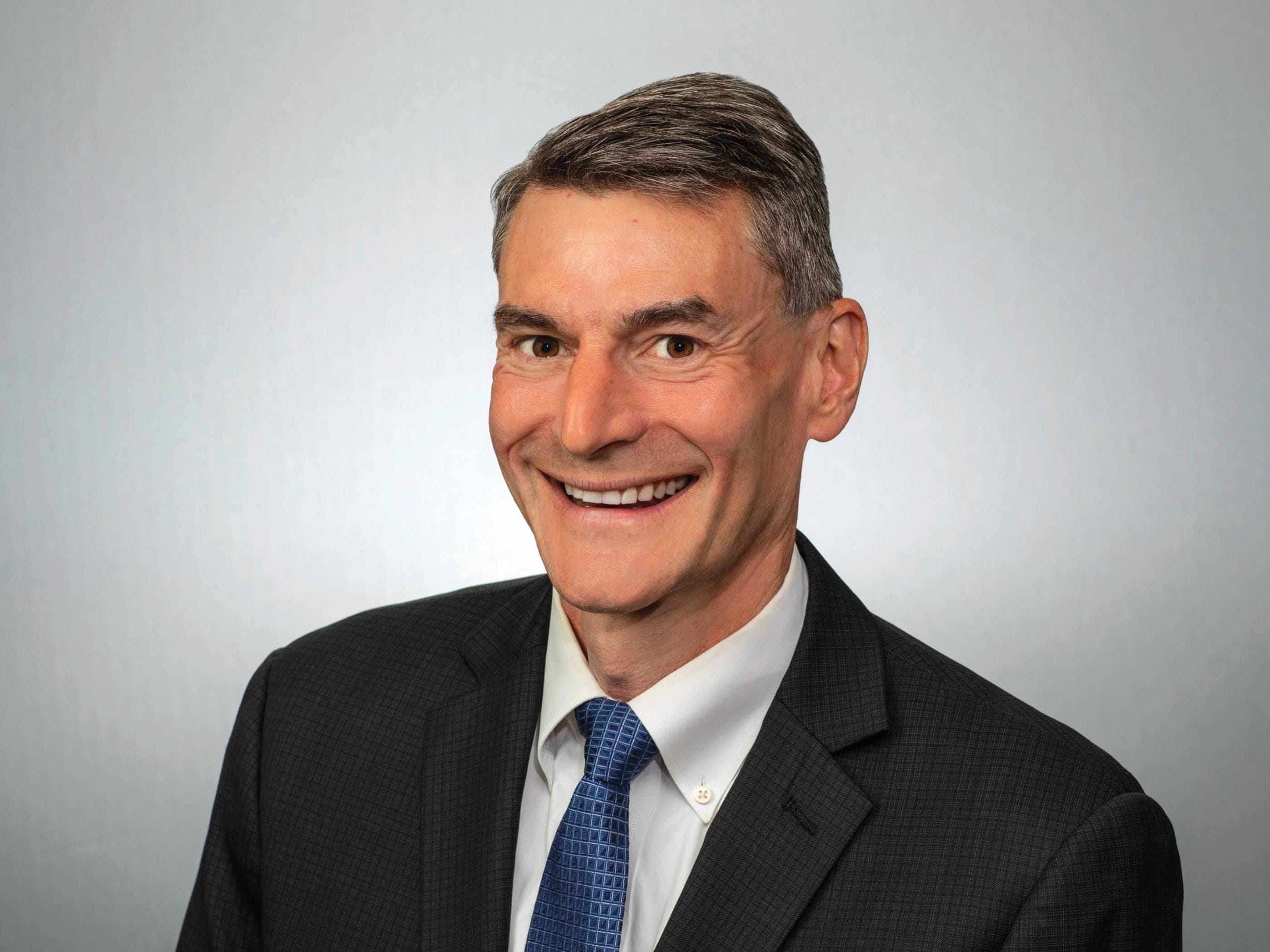 Portrait of a man wearing a black suit jacket and a blue tie.