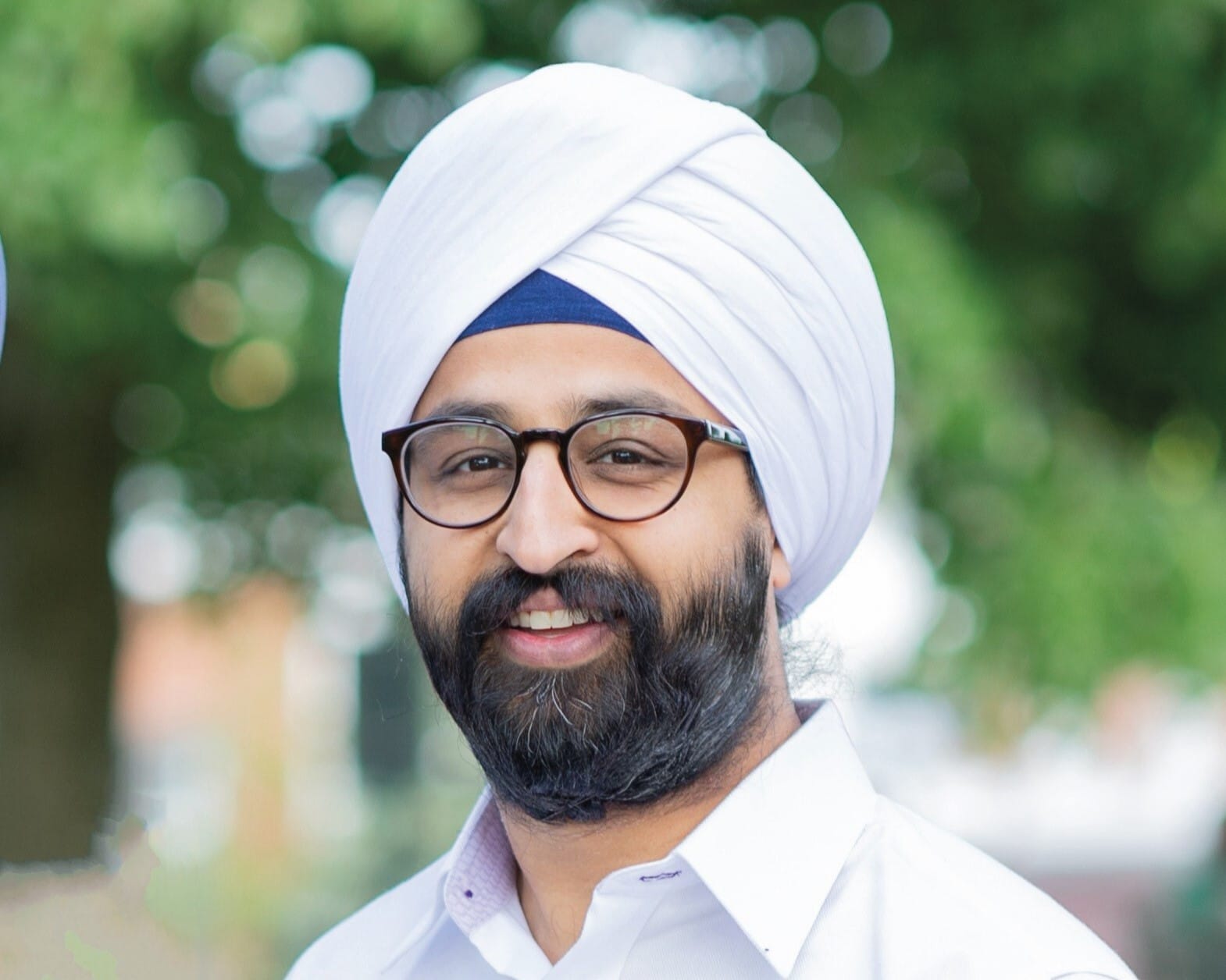 A portrait of a man wearing a dastār (turban), black-rimmed glasses, and a white button-down shirt.
