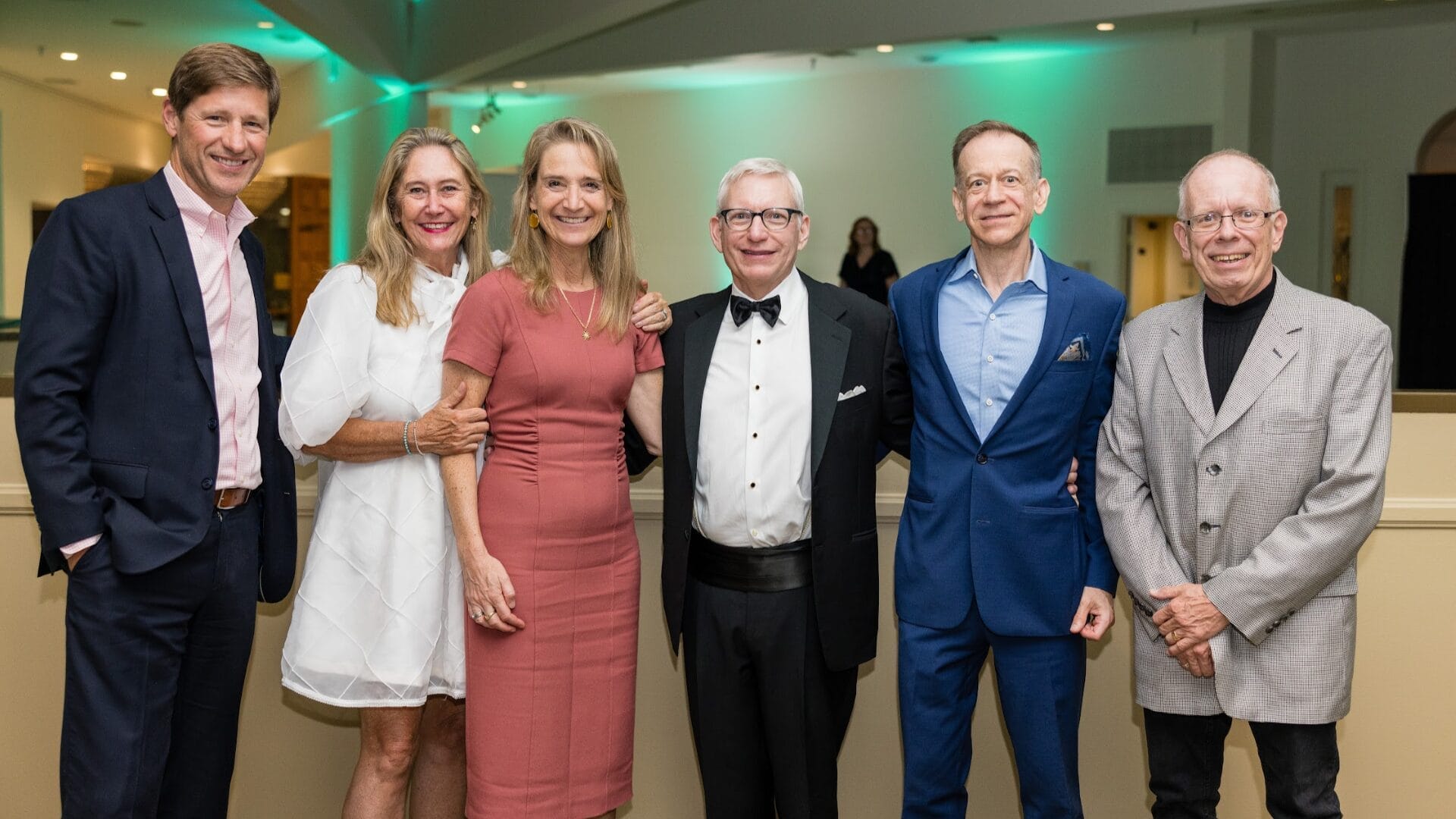 Six alumni pose together in formal wedding attire.
