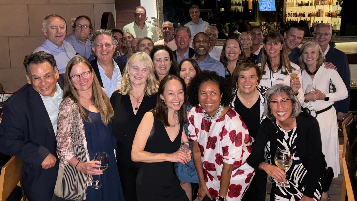 More than two dozen alumni gather together for a photo at a bar.