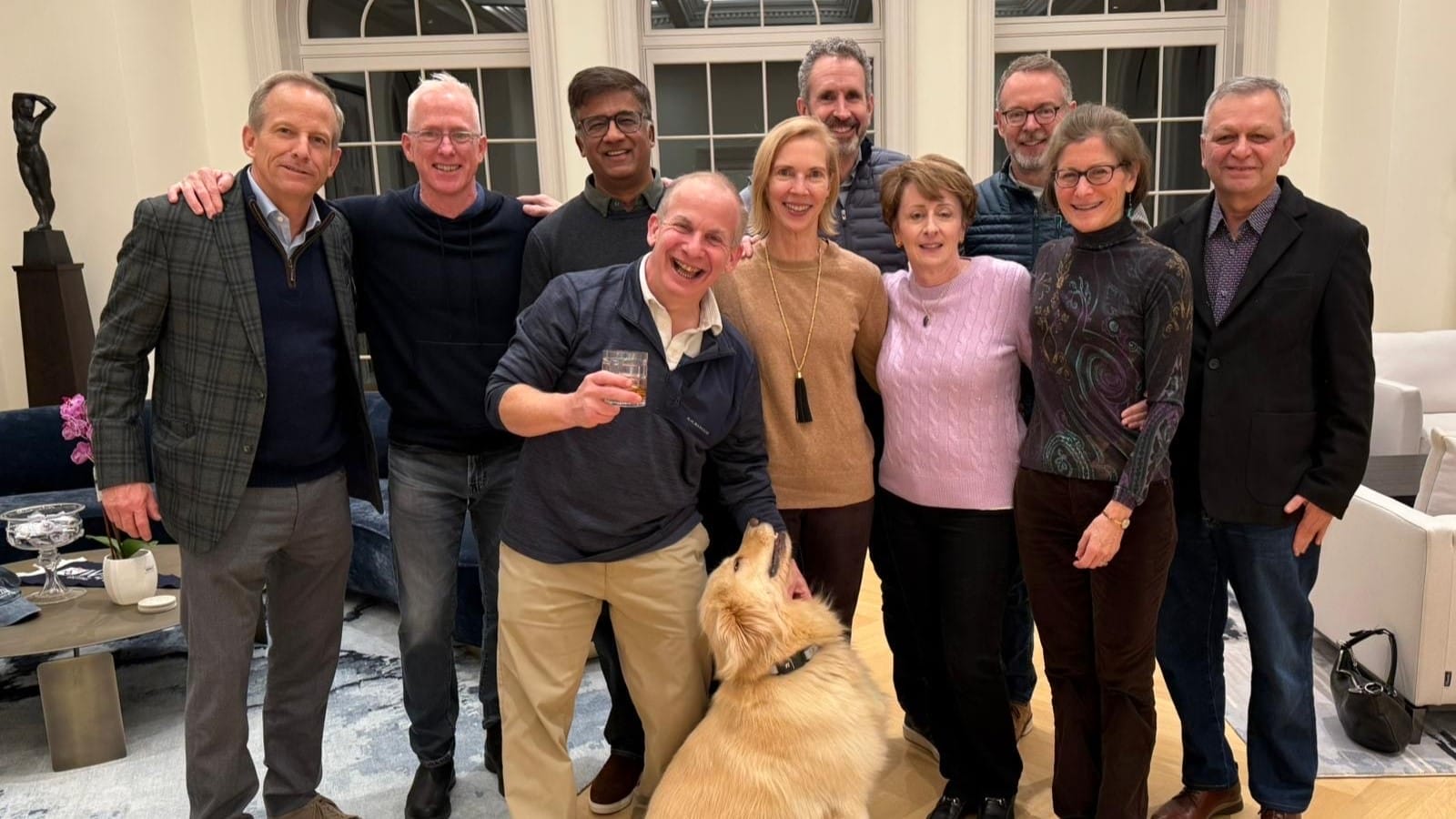 A group of ten alumni in evening attire pose for a picture with a dog sitting in front.