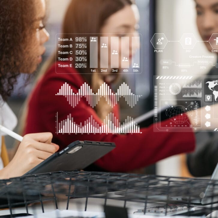 Students working on a project together using a laptop and tablet while graphics hover above them