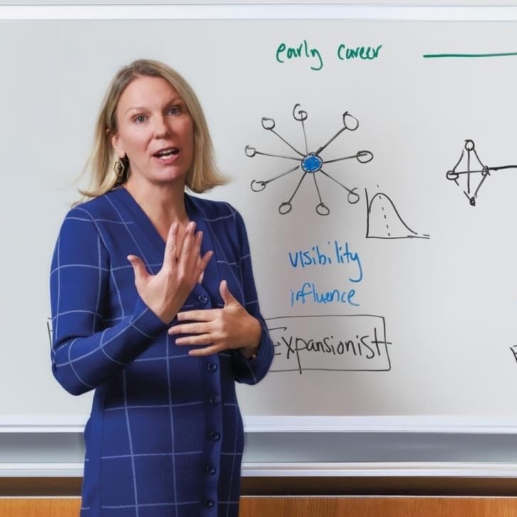 A woman stands in front of a whiteboard in business attire.