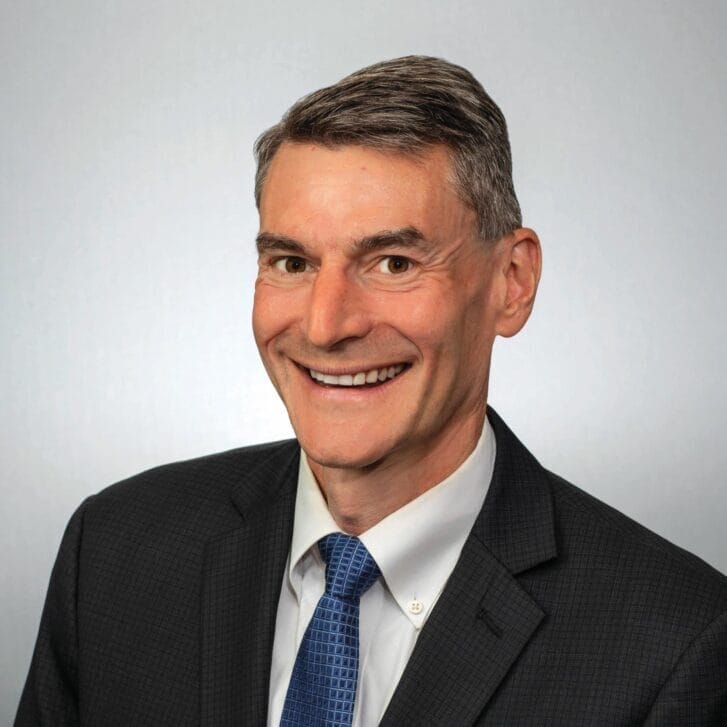 Portrait of a man wearing a black suit jacket and a blue tie.