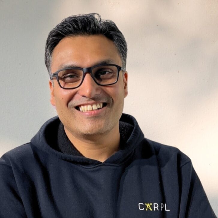 A portrait of a man wearing black-rimmed glasses and a hoodie.