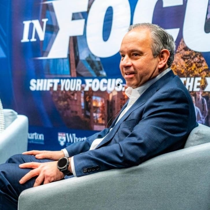 A man and woman seated on a stage in business attire.