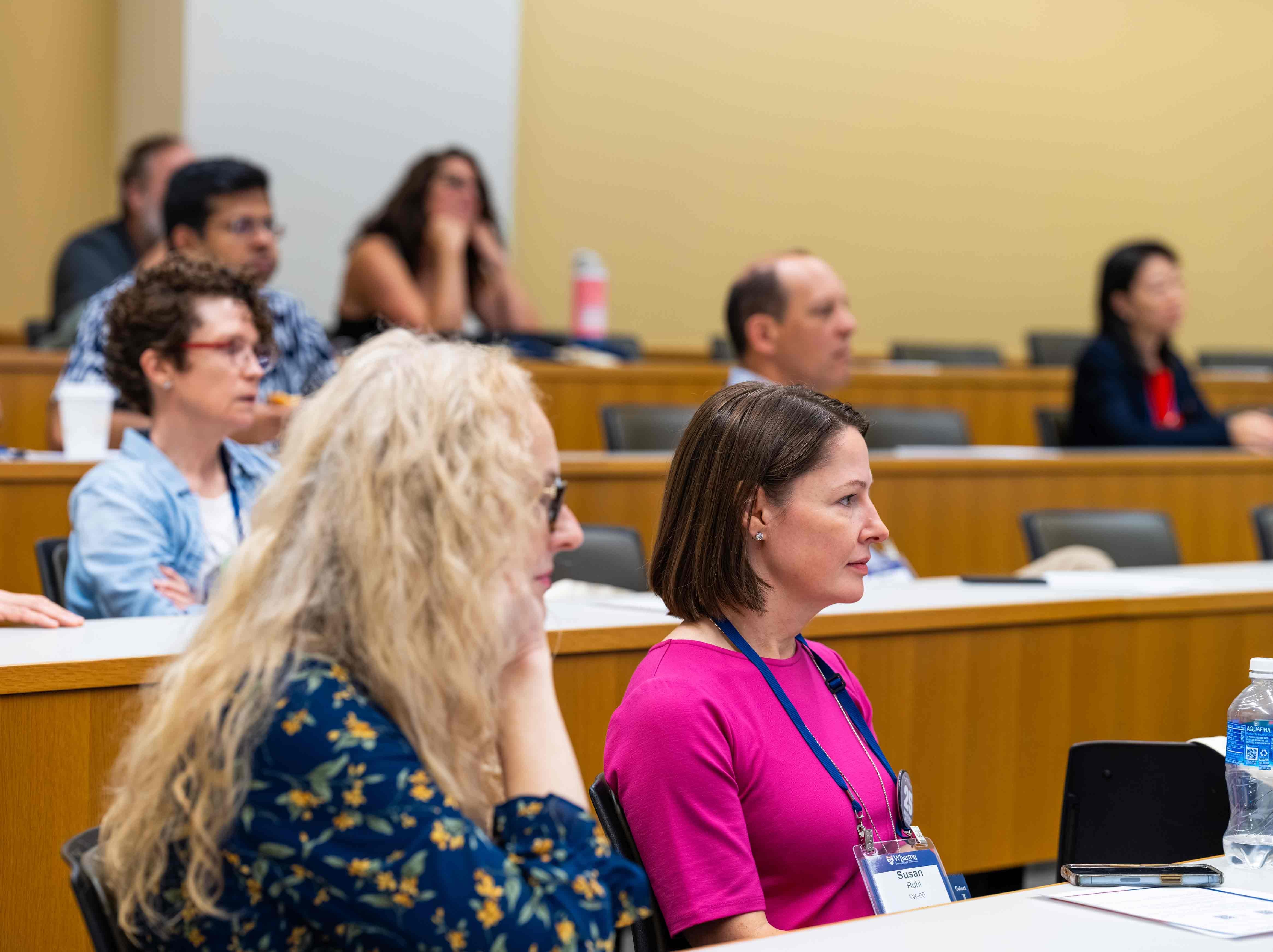 People sit in a tiered classroom, gazing in the same direction.