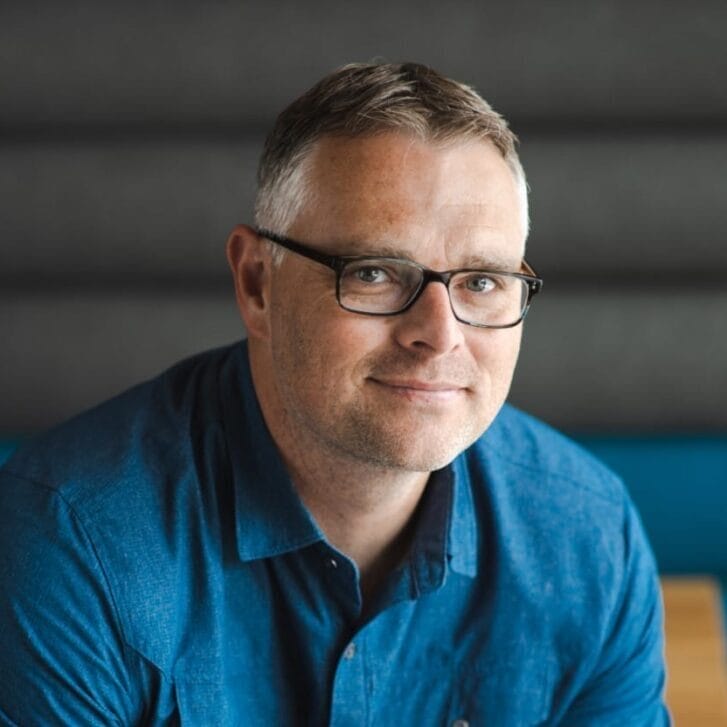 Man wearing a blue button-down shirt and black-rimmed glasses.
