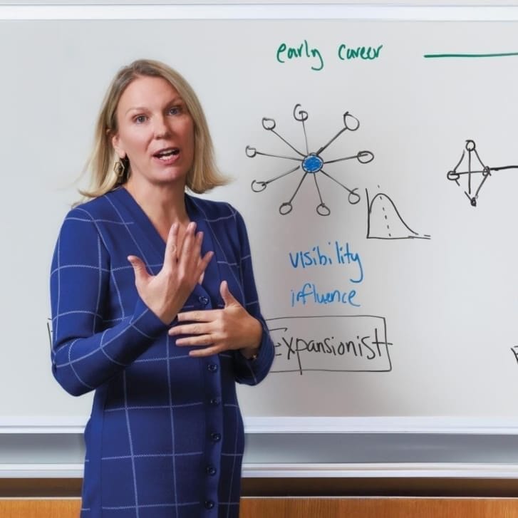 A woman stands in front of a whiteboard in business attire.