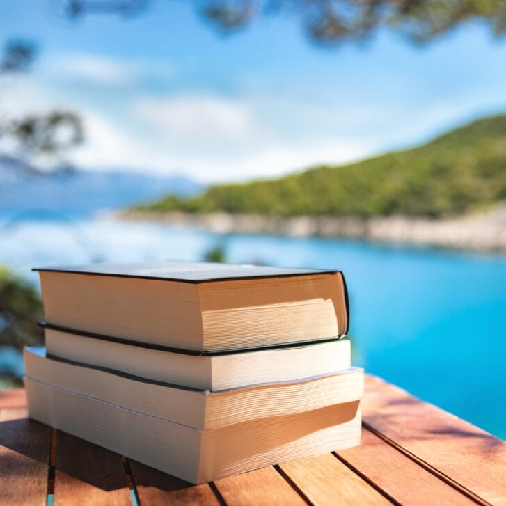 A stack of books rests on a table by the beach.