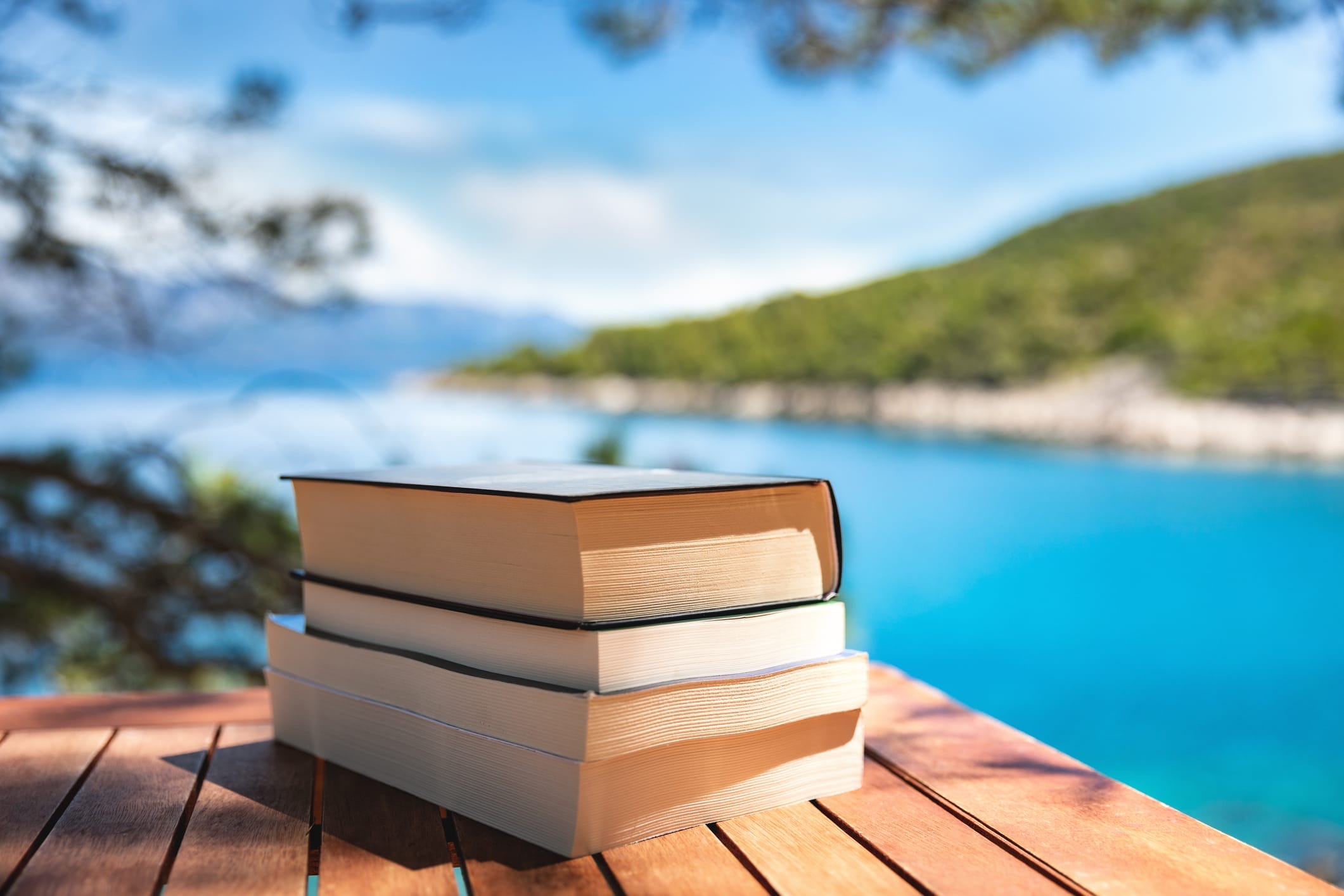 A stack of books rests on a table by the beach.