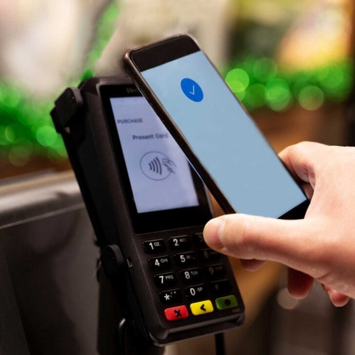 Hand holding up a mobile device to a payment terminal