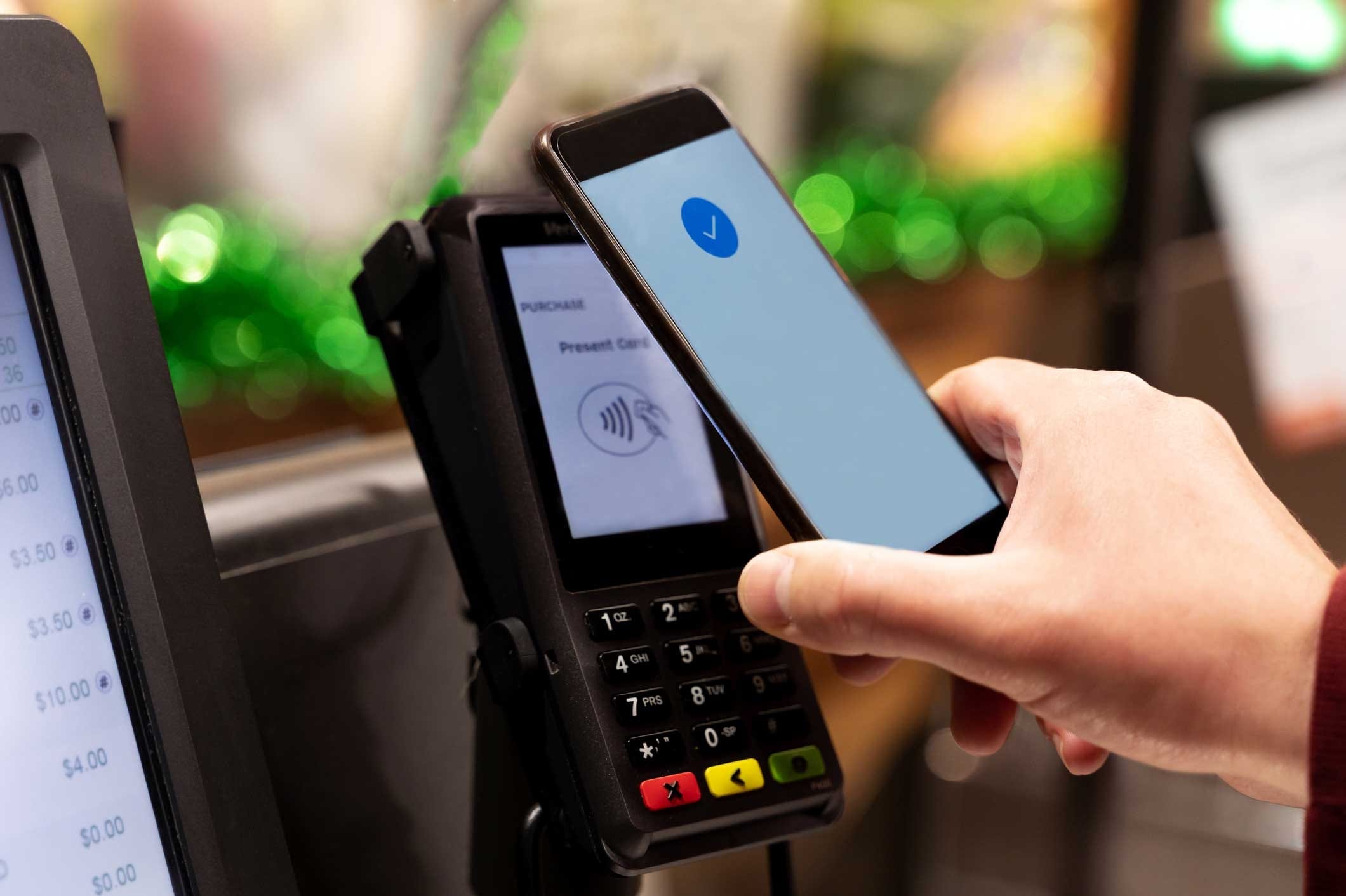 Hand holding up a mobile device to a payment terminal