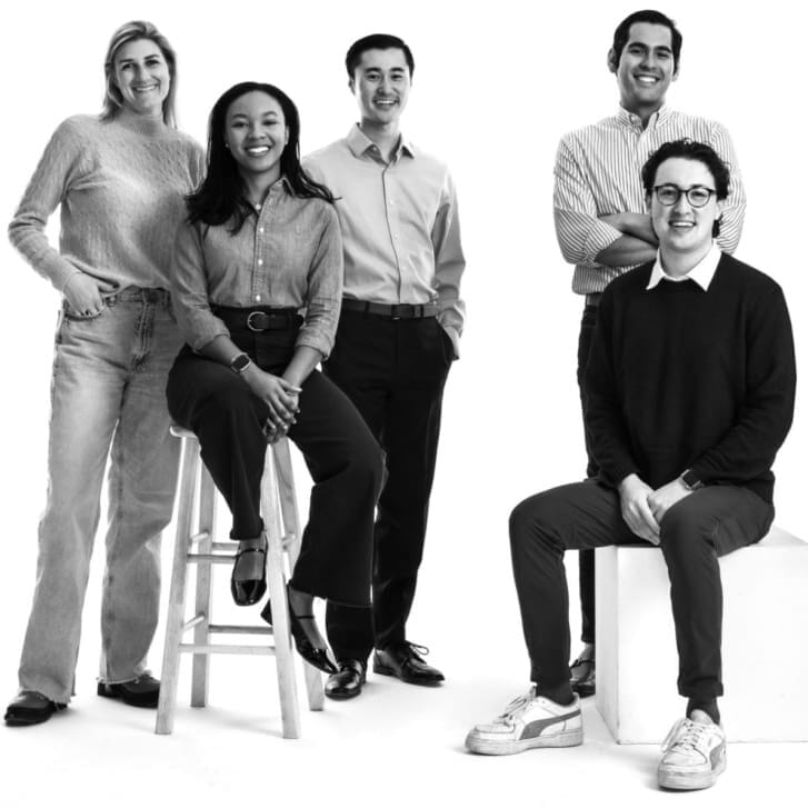 Five students in business-casual attire pose together against a white studio backdrop.