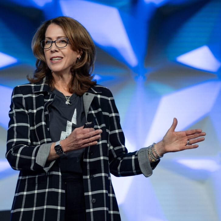 A woman gestures while standing in front of a blue screen