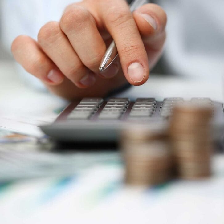Hand performing calculations on a calculator with stacks of coins nearby