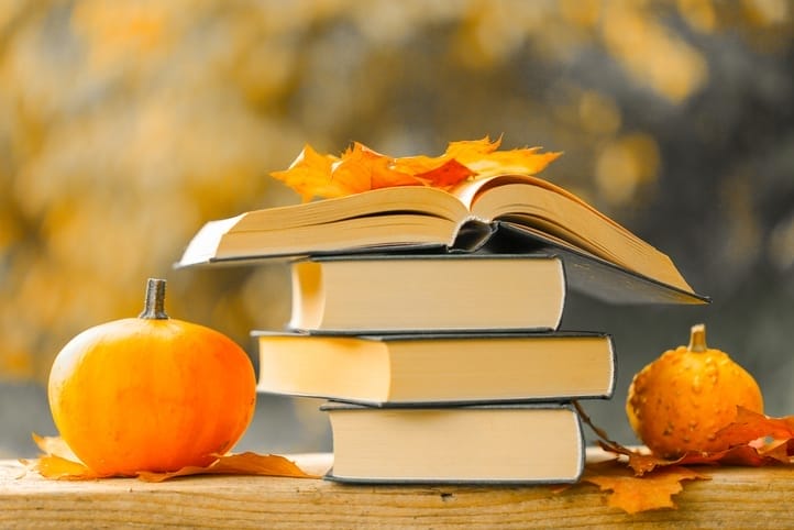 stack of books surrounded by pumpkins and orange leaves