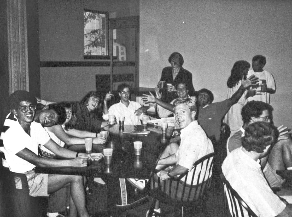 A black-and-white photo of several students seated around a table with drinks.
