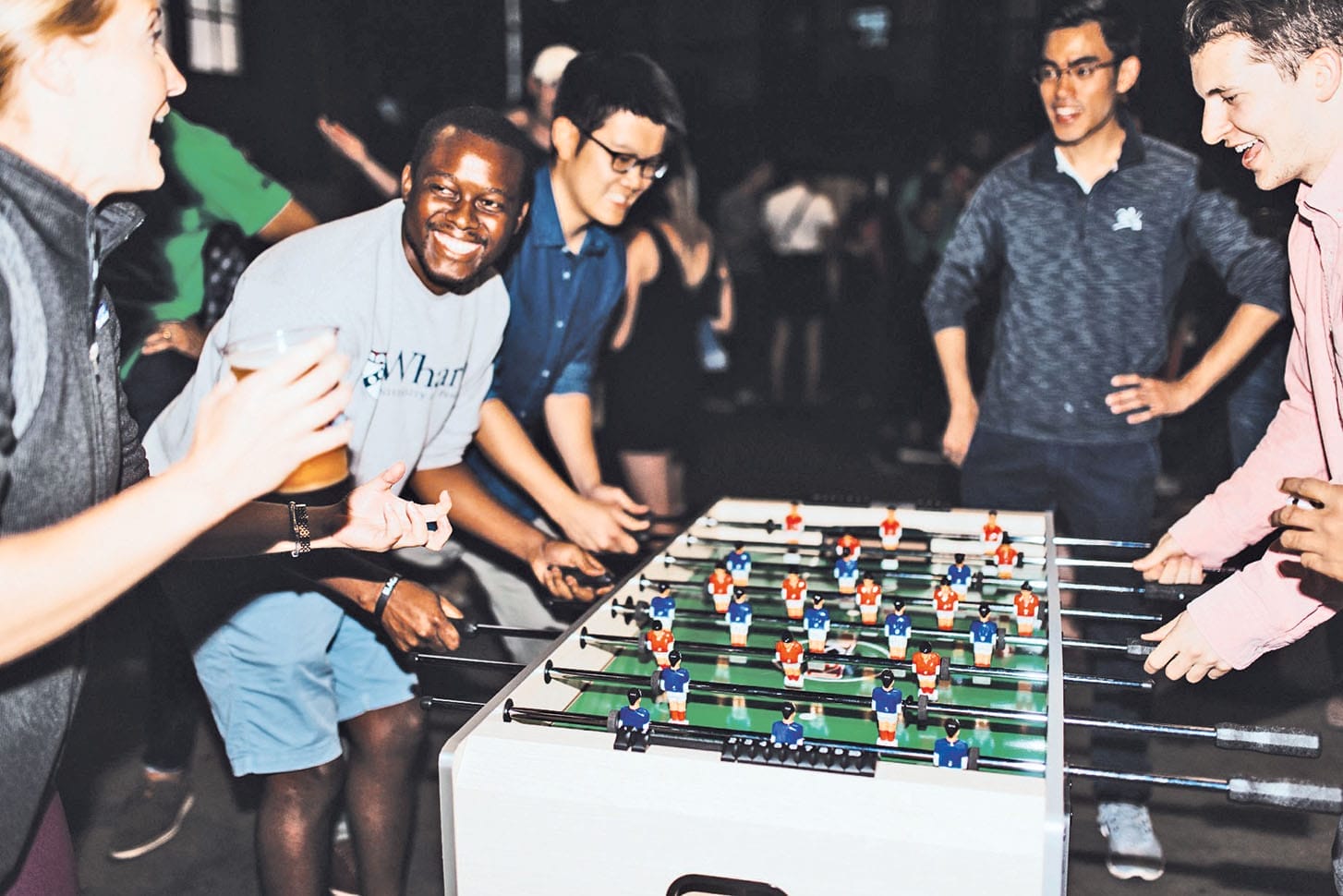 Students in casual attire stand around a foosball table holding the table's handles.