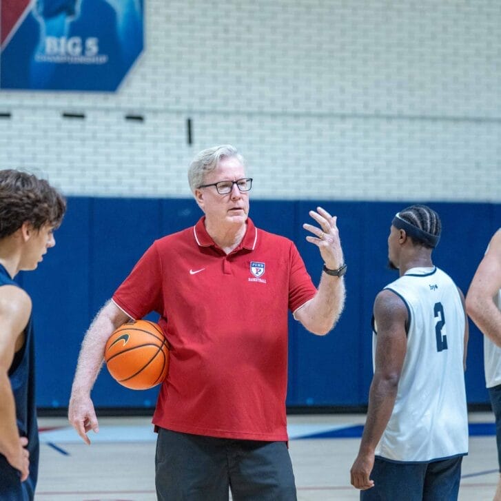Man in a red shirt standing on a basketball court surrounded by basketball players